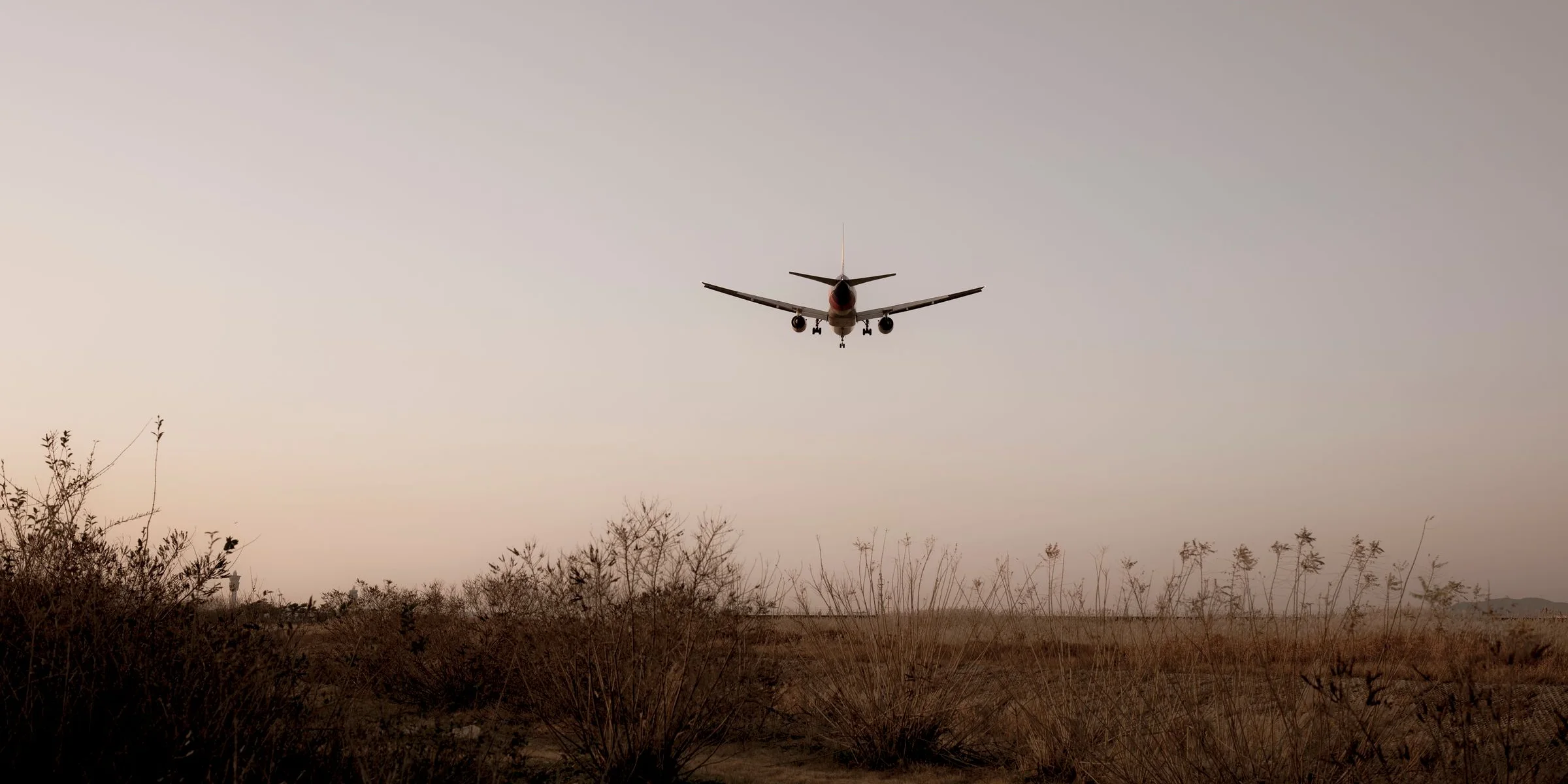 Airliner coming in to land over a grassy field at dusk