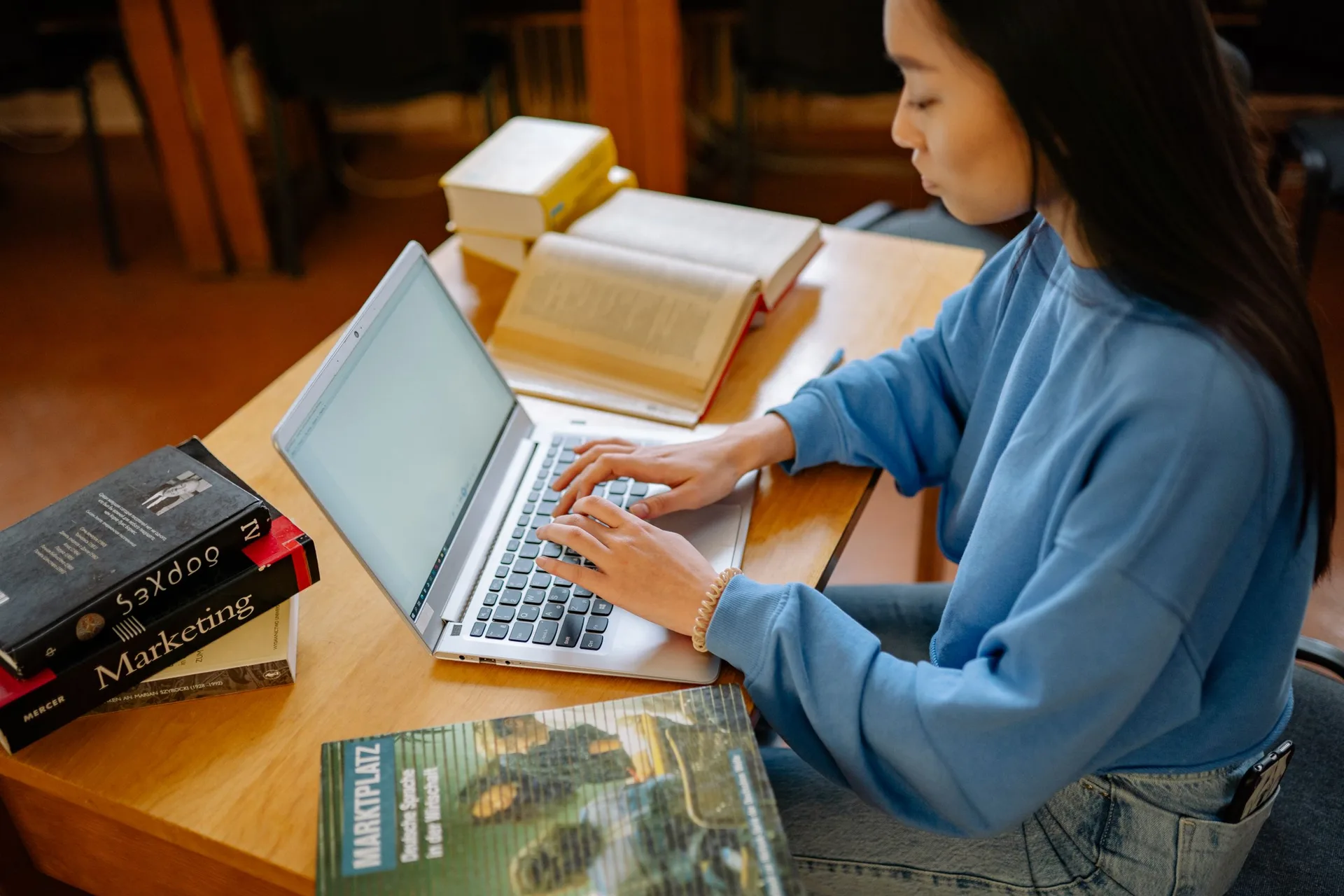 Student typing on a laptop at a desk with books