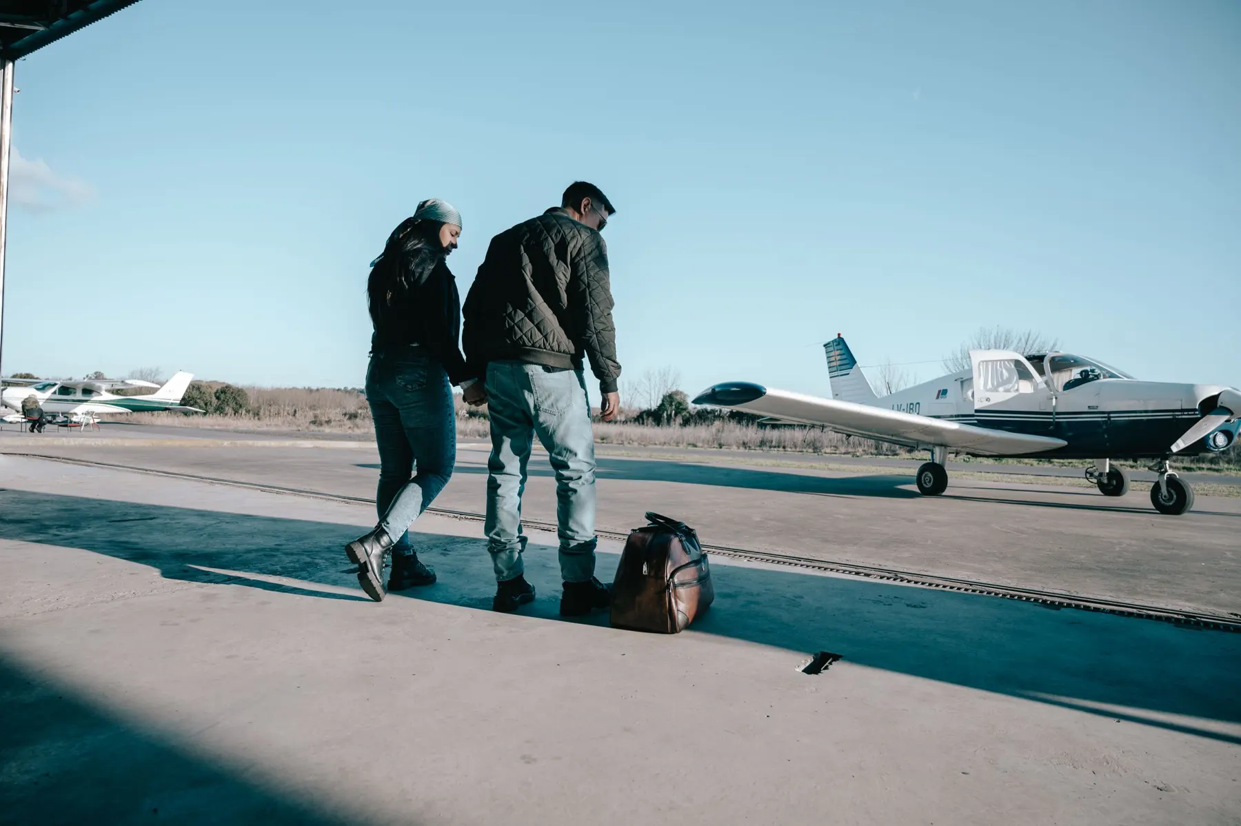 Two people walking with bags towards light aircraft on an apron