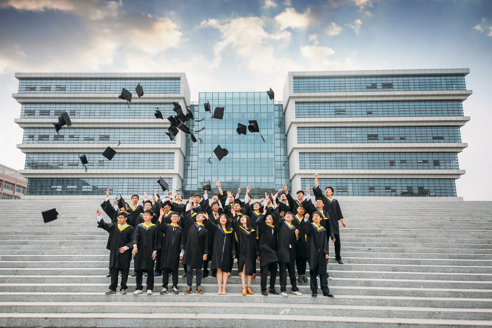 Graduates throwing caps on the steps of a modern campus building