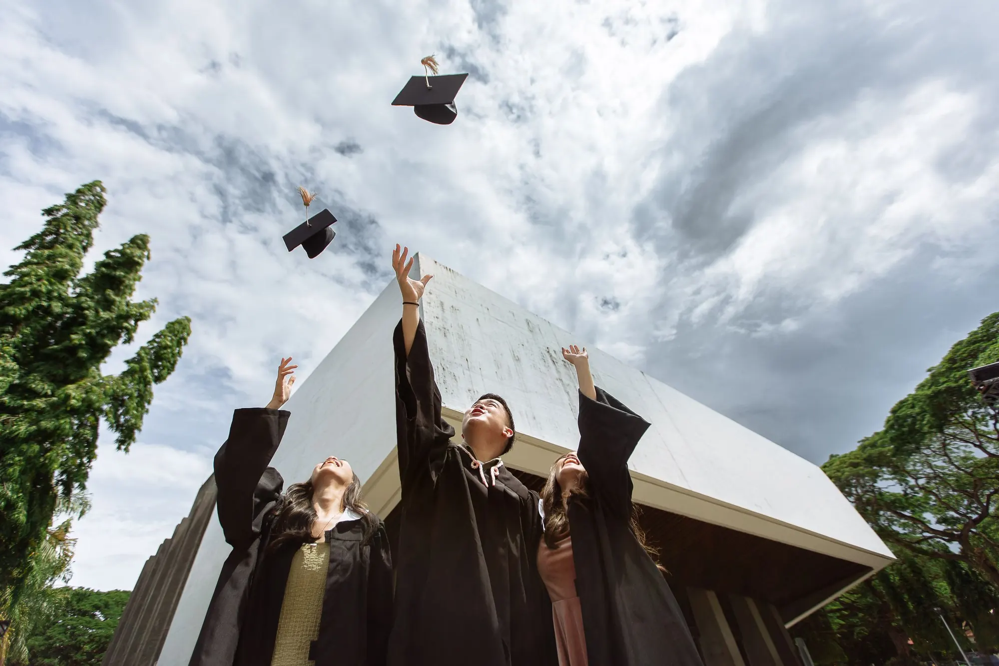 Graduates tossing mortarboards in front of a modern building