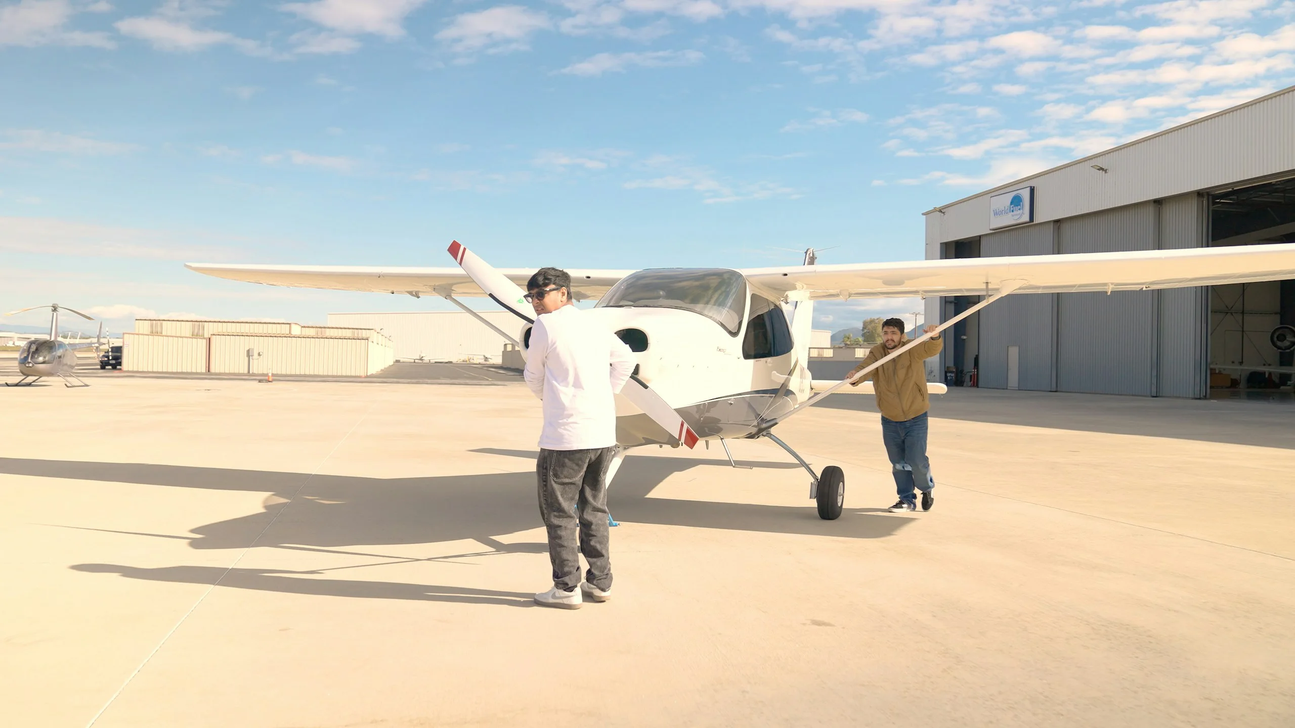Two people walking around a light aircraft on an apron beside a hangar