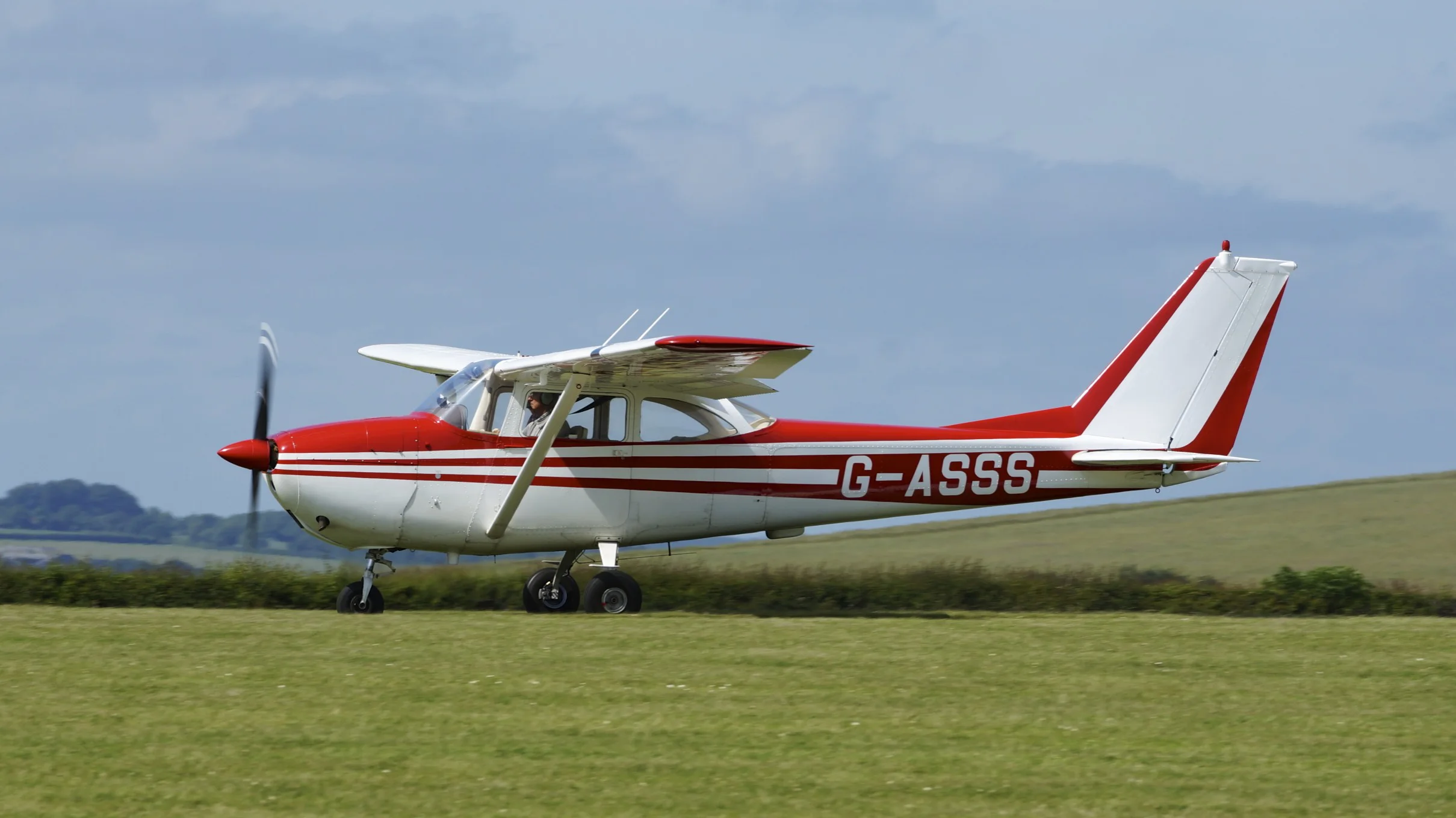 Training aircraft on a grass airfield under a bright sky