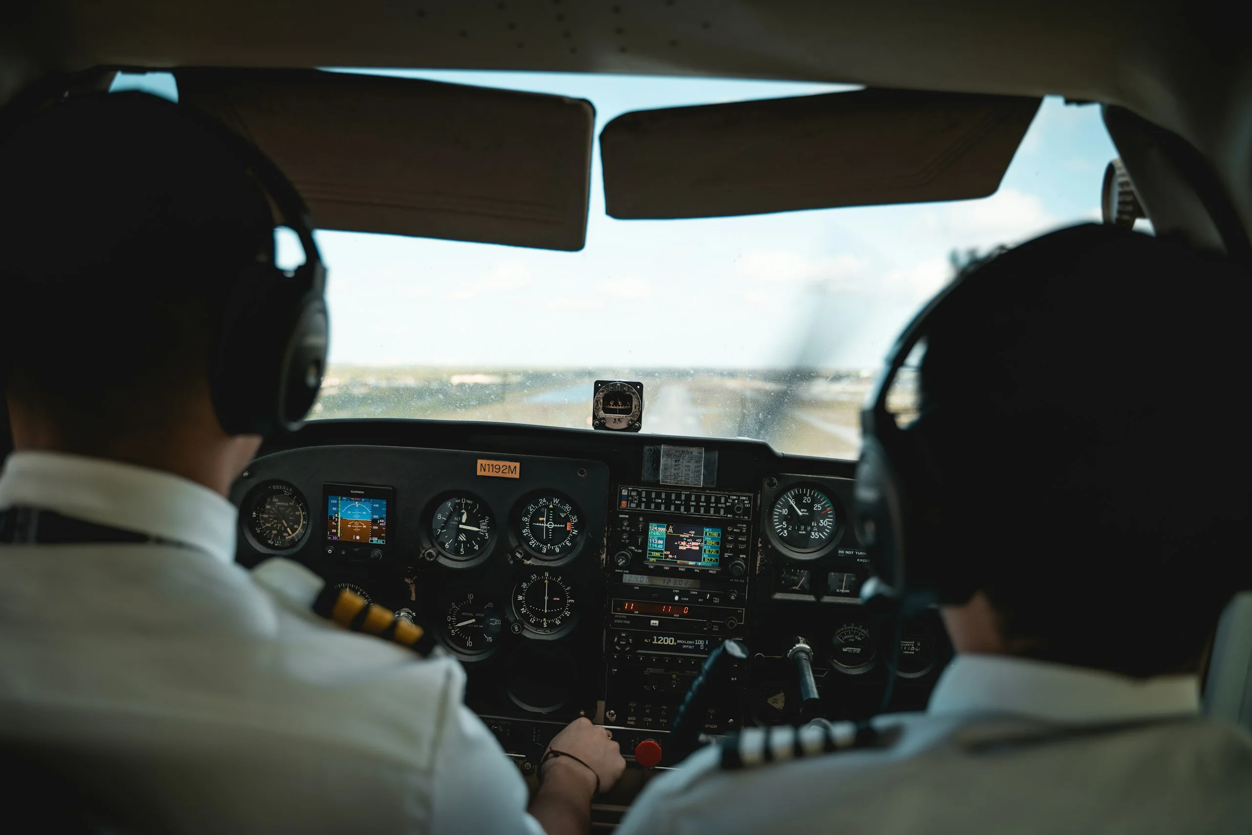 Two pilots wearing headsets in a light aircraft cockpit, seen from behind