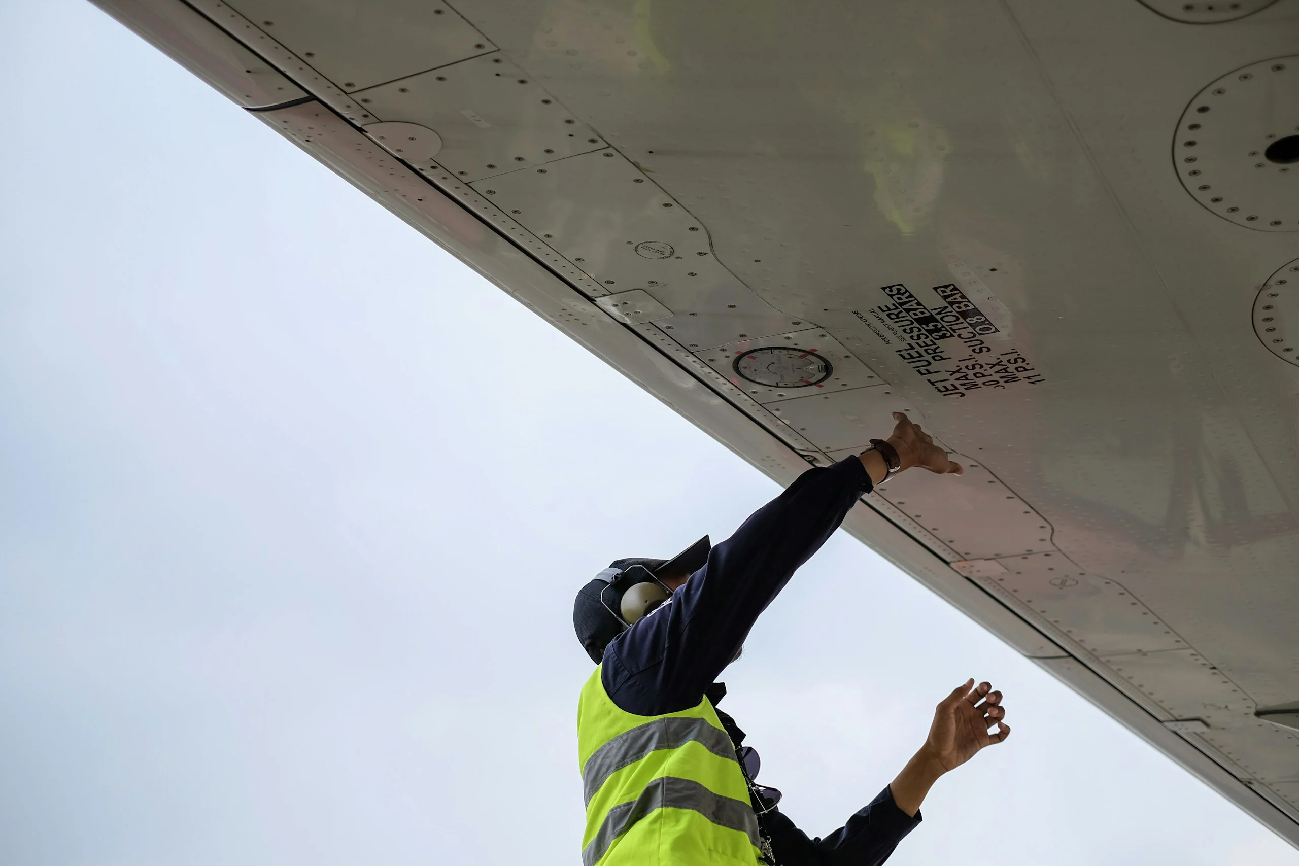 Person in a high-visibility vest reaching up to the underside of an aircraft wing